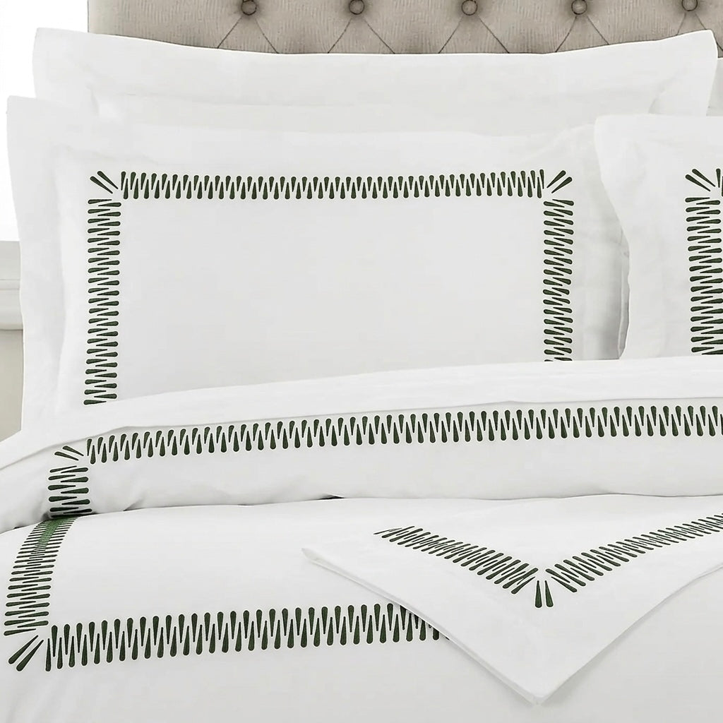 White bedding set with black zigzag border embroidery on the pillowcases and duvet cover, styled on a bed with a tufted headboard.