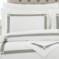 White bedding set with black zigzag border embroidery on the pillowcases and duvet cover, styled on a bed with a tufted headboard.