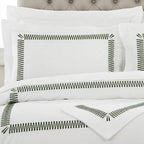 White bedding set with black zigzag border embroidery on the pillowcases and duvet cover, styled on a bed with a tufted headboard.
