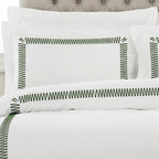 White bedding set with green zigzag border embroidery on the pillowcases and duvet cover, styled on a bed with a tufted headboard.